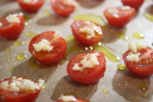Tomaten, Knoblauch und Zwiebeln auf einem Backblech mit Olivenöl beträufeln